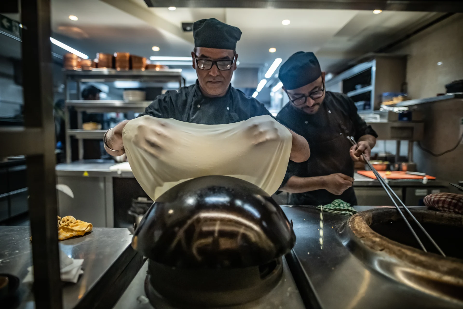 Two chefs stretching naan at the tandoor oven